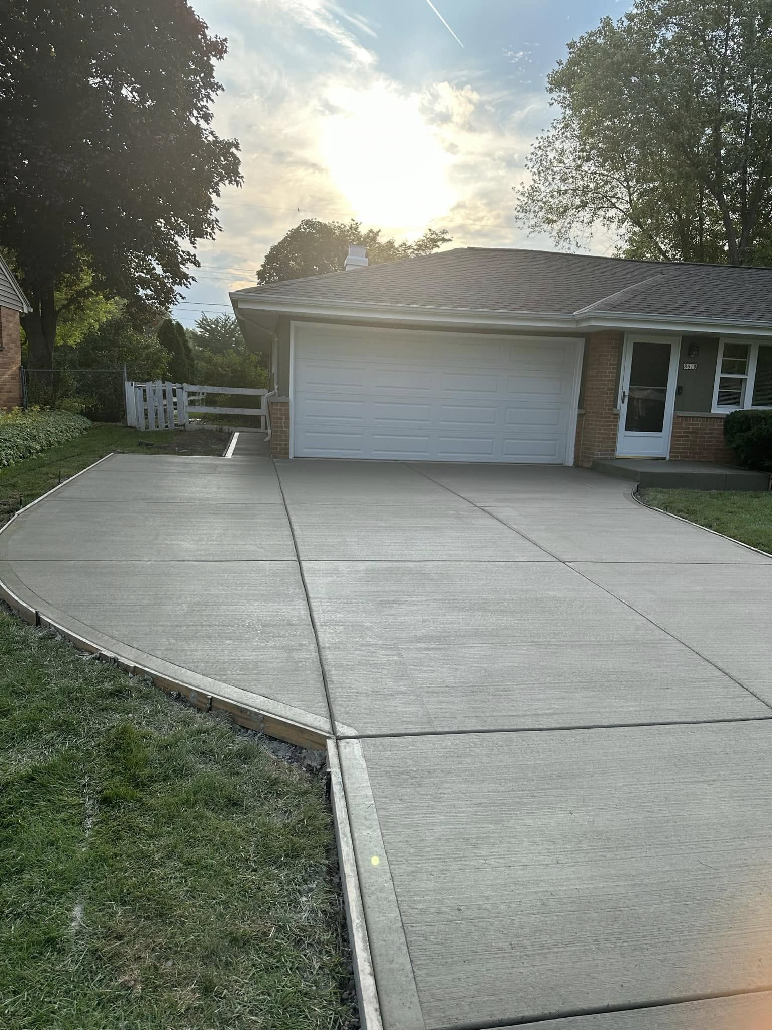 Newly poured concrete driveway with broom-finish texture and control joints leading to two-car garage at dusk